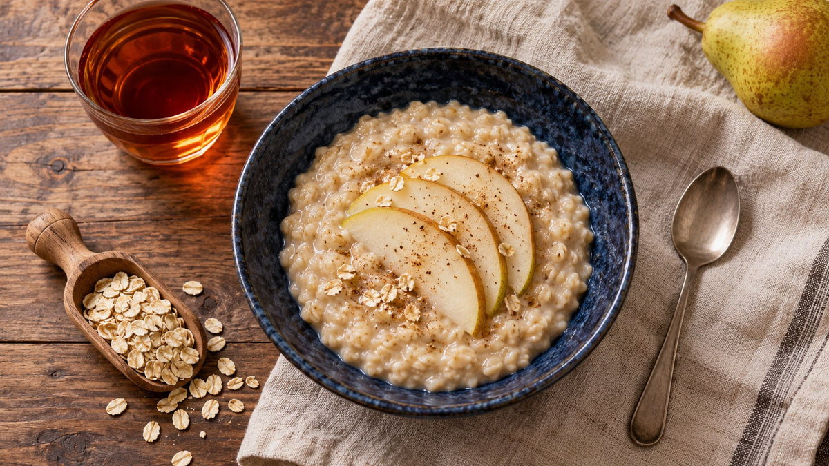 Haferporridge mit Birnenspalten in einer dunkelblauen Keramikschale neben bernsteinfarbenem Rooibos auf Leinen