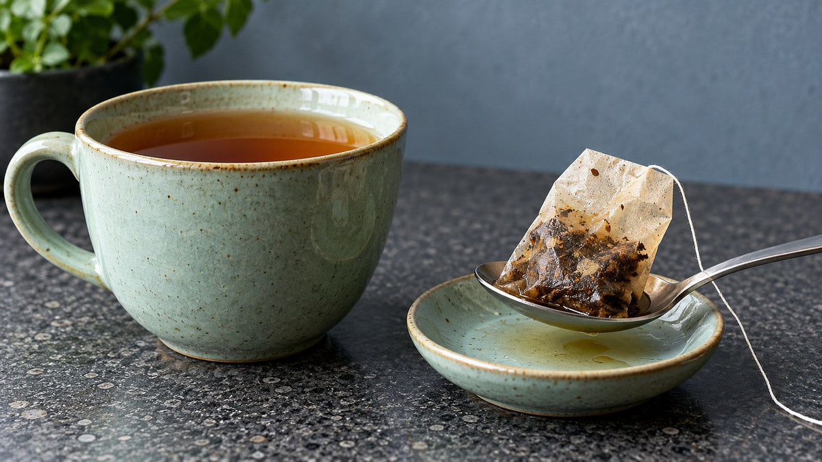 Ein nasser Teebeutel liegt auf einem Löffel neben einer grünen Tasse mit Tee
